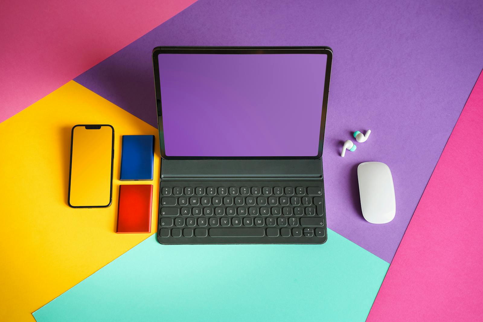 Vibrant flat lay of tablet, smartphone, and mouse on colorful background.